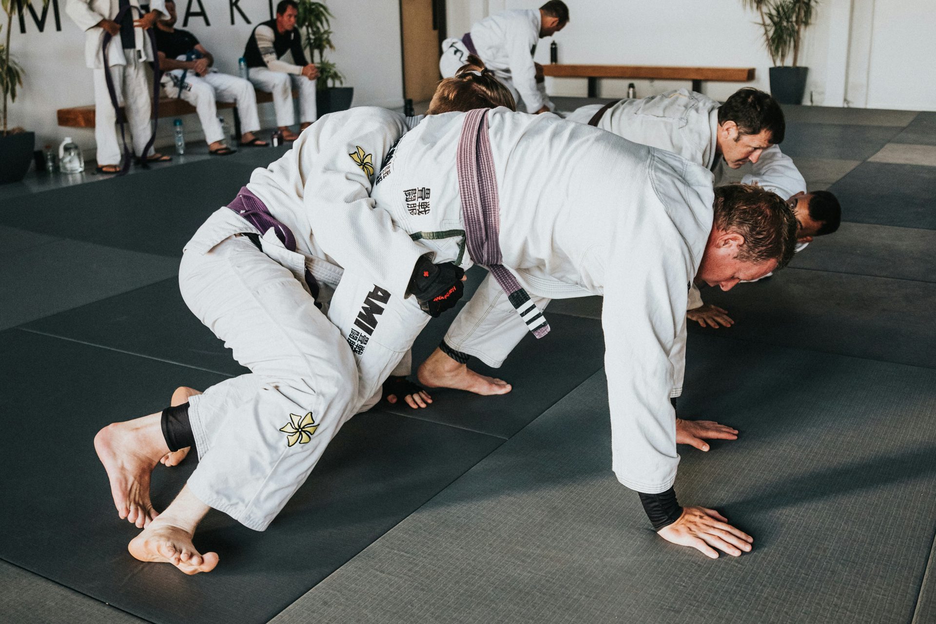 A man in a white and black uniform executes a Brazilian Jiu-Jitsu move on a training mat